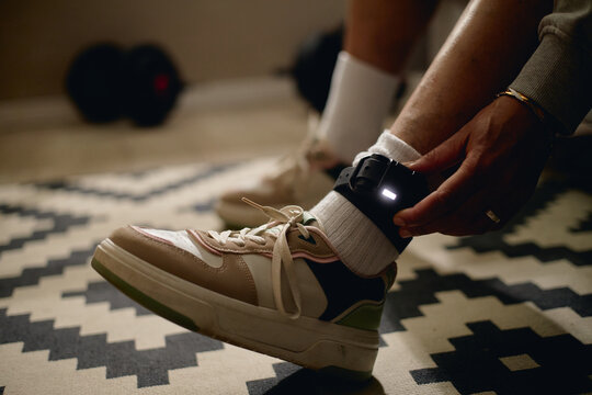 Close up of woman fastening electronic ankle monitor at home, representing house arrest, legal surveillance, restricted freedom. Useful for justice, crime, probation campaigns