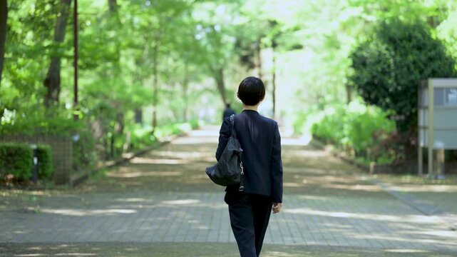 新緑の公園をビジネスバッグを持って歩く女性の営業マンの全身ポートレート仕事イメージ　顔無しの後ろ姿の動画