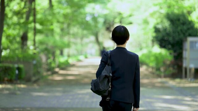 新緑の公園をビジネスバッグを持って歩く女性の営業マンの全身ポートレート仕事イメージ　顔無しの後ろ姿の動画スローモーション