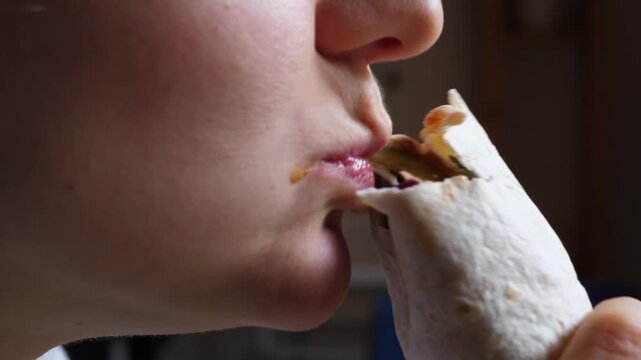 Close up profile of a hungry person taking a big bite and chewing a delicious tortilla wrap. The footage captures the enjoyment of a fast food meal, showing the mouth, lips, and part of the face
