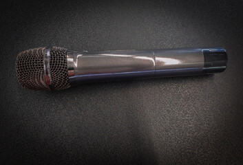 Professional handheld dynamic microphone placed on dark textured background with dramatic lighting Modern wireless microphone with steel mesh head on a textured black backdrop with soft light © Lang