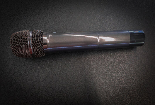Professional handheld dynamic microphone placed on dark textured background with dramatic lighting Modern wireless microphone with steel mesh head on a textured black backdrop with soft light