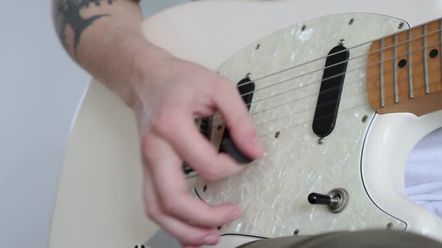 A hand is holding a pick and strumming an electric guitar, the background is neutral.