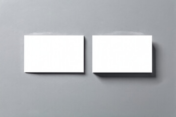 Fototapeta premium Two blank white rectangular cards float above a plain grey background casting soft shadows suitable for various design projects