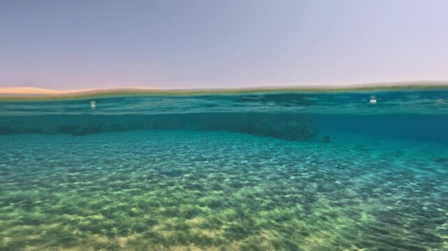Half underwater slow motion view of clear sandy seabed and rolling waves in tropical sea