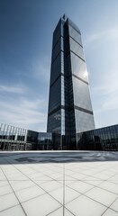 Obraz premium Modern glass skyscraper reflecting sky and clouds in a contemporary urban plaza with geometric paving stones