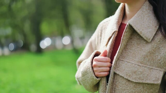 Happy woman smiling while zipping jacket in park. Enjoying fresh air and comfort. Expresses joy and contentment in nature, embracing casual style and warmth during an outing.