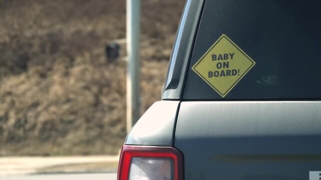 Yellow Baby on Board sign on a car window in city traffic, emphasizing road safety for infants.