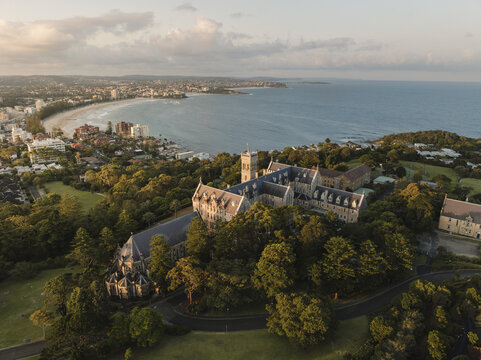 Aerial view of the International College of Management, Sydney featuring gothic architecture and lush greenery with Manly Beach in the background Manly, New South Wales, Australia.