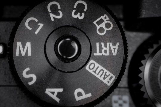 Macro closeup of camera mode dial with PASM settings and auto icons showing textured metal control and photography interface detail