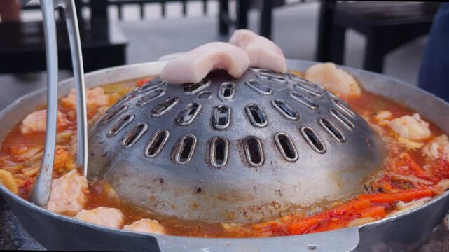 Thai BBQ Hot Pot with Dome Grill Simmering in Spicy Broth, Close-Up