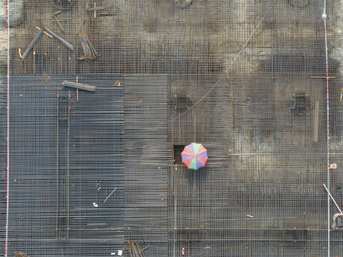 Aerial view of a construction site featuring a dense grid of steel rebar mesh with a colorful umbrella and workers on the ground in Taiwan.