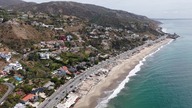 Cinematic daytime aerial drone footage captured at an angle along the California coastline, featuring the iconic Pacific Coast Highway running parallel to the shoreline.