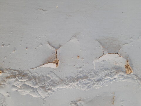 Close-up view of cracked, textured wall with spalled sections on a wall surface. Cracked wall with severe bubbling and peeling due to moisture.
