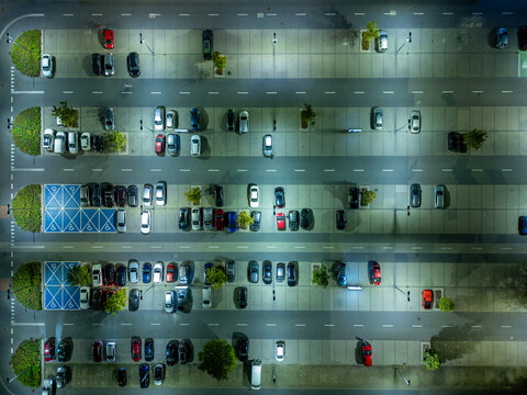 Aerial view of a parking lot at night with rows of cars illuminated by streetlights and blue handicapped parking spaces Warsaw, Masovian Voivodeship, Poland.