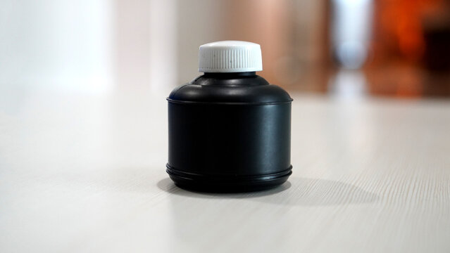 Small black refill ink bottle with white lid for inkjet printer cartridge maintenance and office stationery supply on white table background for professional printing and digital imaging service.