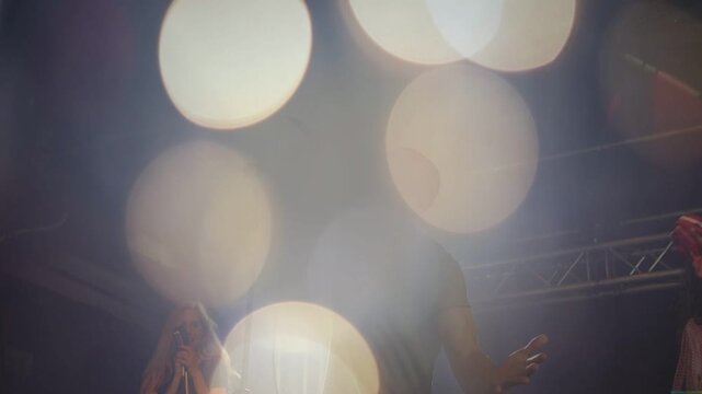 Lead singer raising arm cueing high note on music stage, duo singing bokeh obscuring then clearing