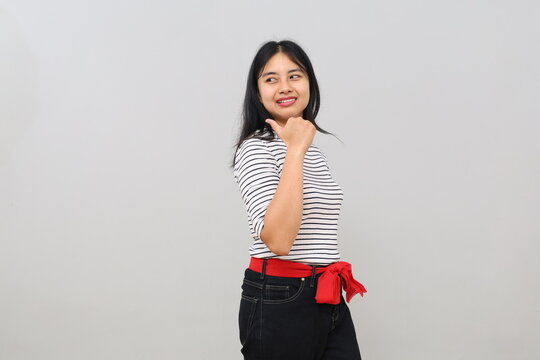 A happy, smiling Asian woman, pointing with her thumb sideways towards empty space, isolated on a white background.