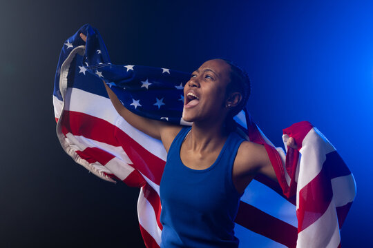 African American female holding American flag, shouting, wearing royal blue sleeveless top on stage