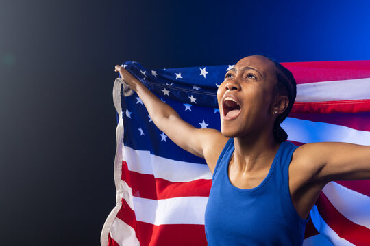 African American woman wearing blue athletic tank top holding US flag in studio, cheering