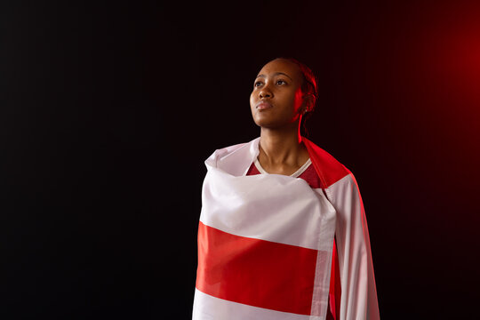 African American woman standing wrapped in red-and-white striped flag in studio, gazing upward