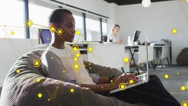 Woman on beanbag typing laptop, causing yellow hex nodes and lines multiplying around tech office