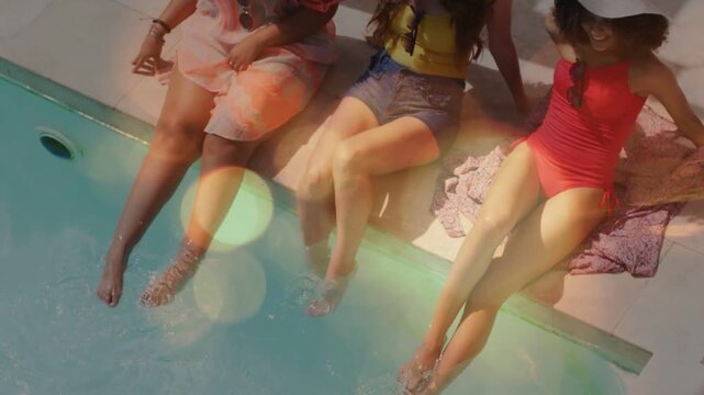 3 women sitting poolside, camera pulling back, bokeh overlay accenting hats, splashing feet for ads
