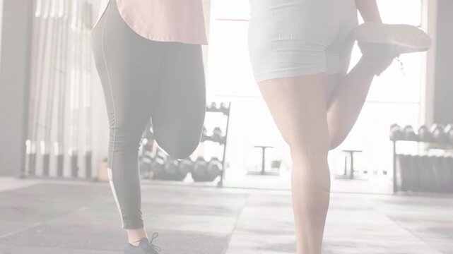 Two women starting warm-up in gym by holding ankle, balancing and adjusting stance near weights