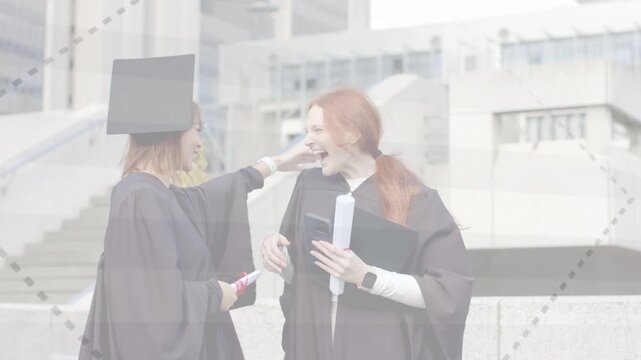 Two grads checking phone on campus steps, friend lifting cap, hugging, celebrating graduation