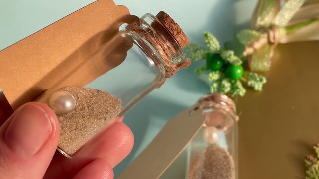 Hand holding small glass souvenir bottle with sea sand pearl and craft tag, wedding favors and summer memory concept