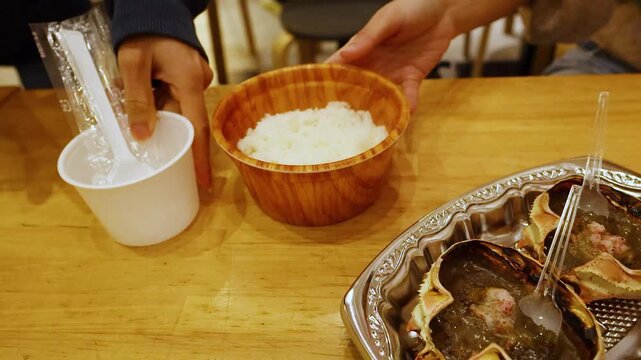 Serving traditional grilled crab shells with miso and white rice on wooden table in Japanese market.