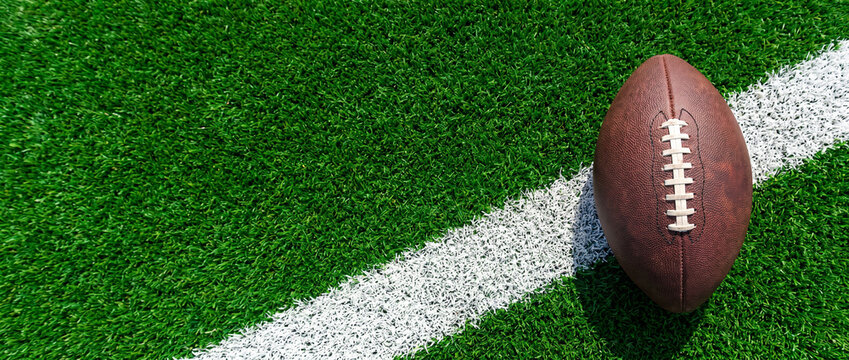 American football resting on yard line of green turf field.