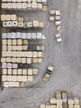Aerial view of stacks of wrapped cargo pallets and forklifts operating on a concrete industrial yard in Taiwan.
