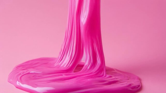 Female hand stretching a sticky, glossy pink slime against a matching pink background