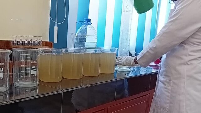 Water Treatment Technician in Lab Coat Filling Beakers with High Turbidity Raw Water for Jar Test Analysis