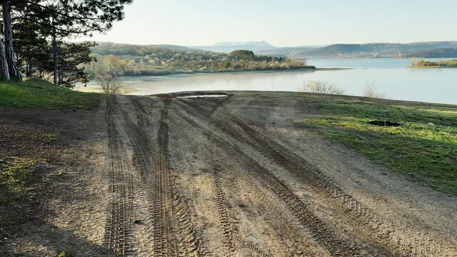 A rugged dirt road leads toward a calm lake and distant hills. This scenic overlook feels peaceful and adventurous. The soft morning light creates a serene and hopeful mood.