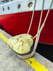 Fototapeta premium Rope tied to a yellow fender with a large ship in the background at the dock during daylight hours
