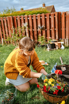 Child girl gardening with flowers in backyard near wooden fence