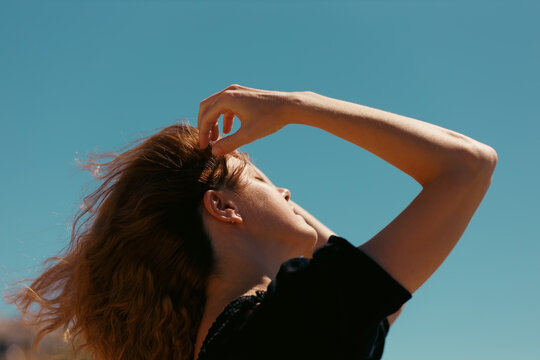 Carefree young woman raising hand in hair against blue sky