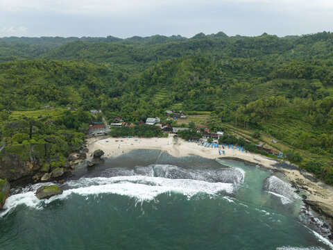 Aerial view of Siung Beach featuring white sand, turquoise waves, and lush green tropical hills in Tepus, Special Region of Yogyakarta, Indonesia.
