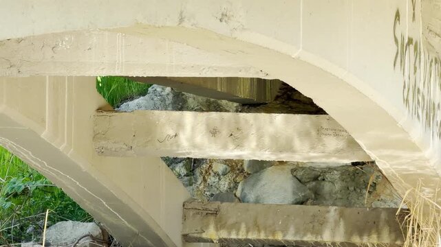 Weathered concrete arches and beams provide a solid frame over a rocky natural landscape. The scene feels quiet and hidden, showing the contrast between heavy construction and the wild outdoors.