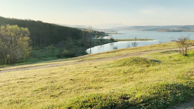 Grassy hills roll down to meet the quiet waters of a large lake under a soft morning sky. This open landscape feels peaceful and free. It is a refreshing scene that brings a sense of calm.