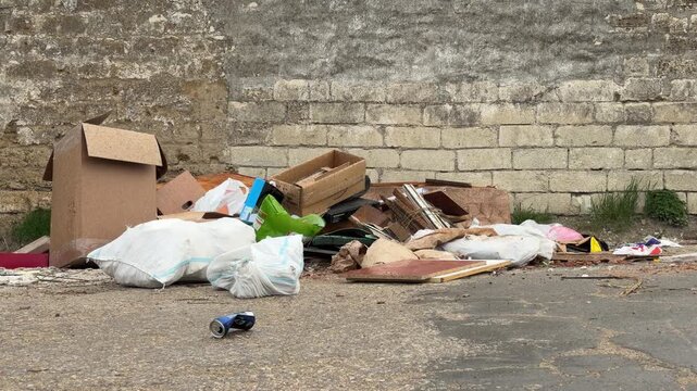 Discarded boxes and white sacks clutter the worn pavement. This messy scene creates a feeling of sadness and neglect in the urban alley. It looks lonely and forgotten.