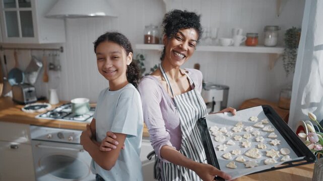 Home bakery, joyful black woman and girl smiling to camera, holding raw cookies. Portrait of happy african american mother and daughter baking tasty homemade sweets for family dinner, look at camera