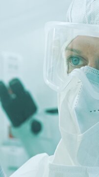 A person in a cleanroom, wearing a full-face mask and protective gear, focuses intently in a sterile medical laboratory setting.