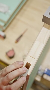 Close-up vertical shot of a carpenter&rsquo;s hand carefully inserting a component
into a precisely cut mortise groove in a wooden door frame. The rectangular cavity is cleanly chiselled.