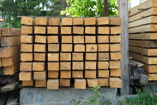 End view of pine timber beams stacked for drying. Raw construction materials arranged in rows at lumber yard with visible wood grain and texture