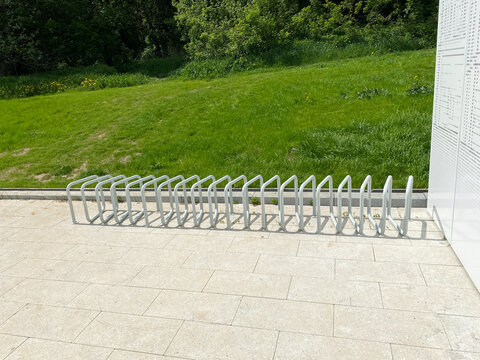 Modern empty bicycle rack on a stone pavement near green park hill. White metal bike stand located in public urban space.