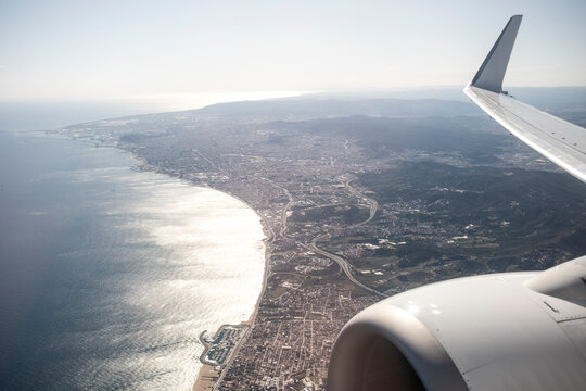 Airplane wing frames Maresme coastline and sea in Catalonia Spain creating aerial travel perspective for commercial transportation imagery