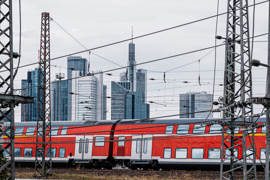 Commuter train passes railway tracks under cables near central station with Frankfurt Germany skyline showing modern transportation infrastructure